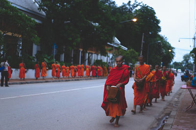 Rear view of people walking by trees against sky