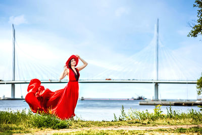 Rear view of woman with arms raised standing on field against sky