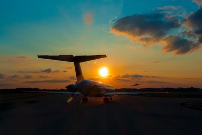 Airplane on runway against sky during sunset