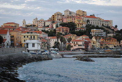 View of buildings by sea against cloudy sky