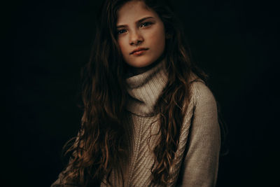 Close-up portrait of young woman against black background