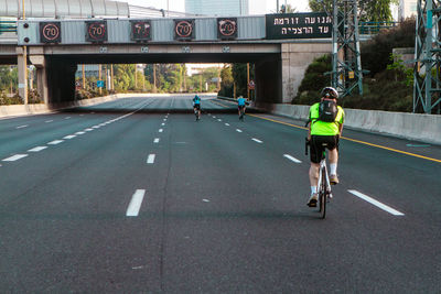 Rear view of man riding bicycle on empty highway. approaching overpass 