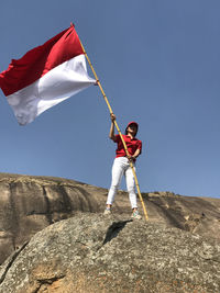 Full length of young woman holding flag standing against sky