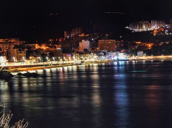 Illuminated buildings by river against sky at night