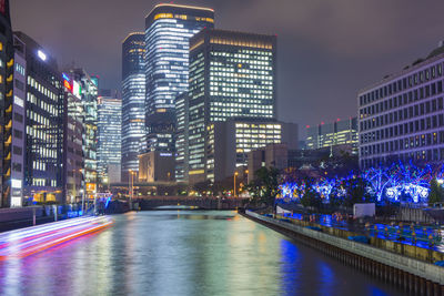 Illuminated buildings by river against sky at night