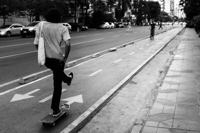 Rear view of man skateboarding on road in city