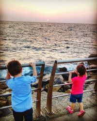 Rear view of boys standing on beach against clear sky