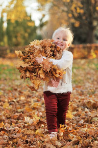 Smiling girl carrying autumn leaves while walking in park