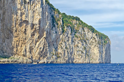 Scenic view of sea by mountain against sky