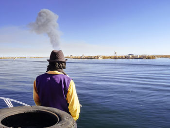 Rear view of man at river against clear sky