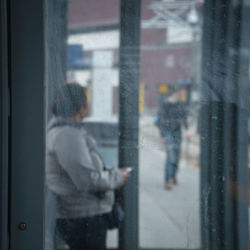 Side view of person at bus stop seen through window