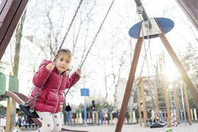 Low angle view of woman standing on swing at playground