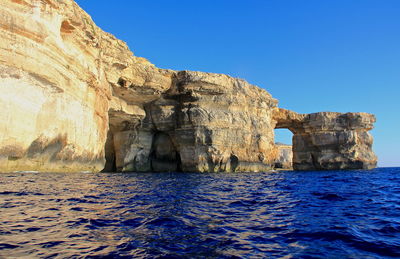 View of rock formation in sea against blue sky