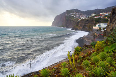 Scenic view of sea by mountain against sky during sunset