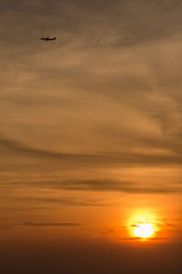Silhouette airplane flying against orange sky