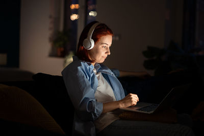 Positive freelancer woman working laptop home late night listening music with headphones.