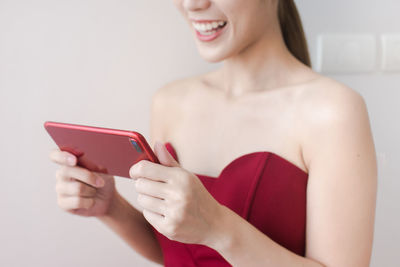 Midsection of young woman using smart phone while standing against wall