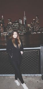 Woman standing by railing against buildings at night