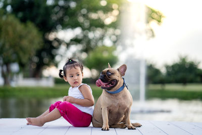 Girl sitting by dog looking away against fountain