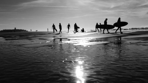 Silhouette people on beach against sky during sunset