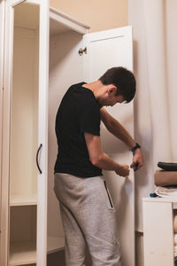 A young man installs handles on the white wardrobe doors.