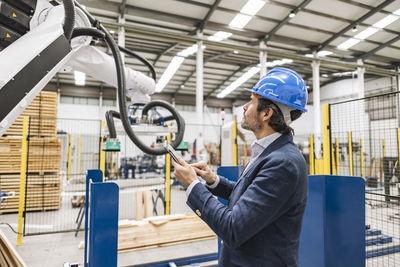 Engineer examining robotic arm using tablet computer in factory