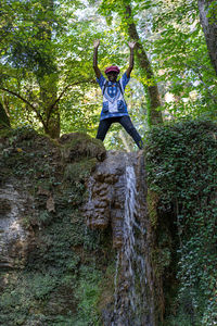 Low angle view of man jumping on rock in forest