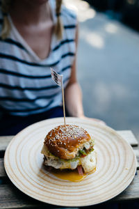 Midsection of woman sitting by plate with burger