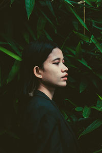 Side view of young woman looking away while standing by plants