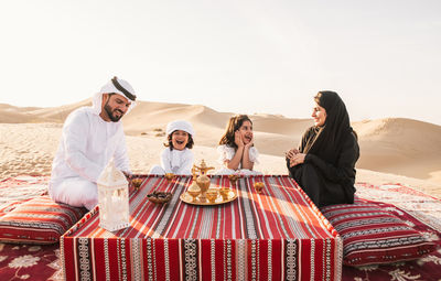 Happy family having tea on carpet at desert