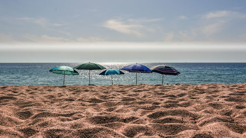 Colorful parasols at beach against sky