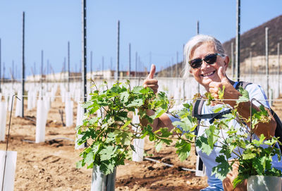 Portrait of smiling woman showing thumbs up with sunglasses against plants