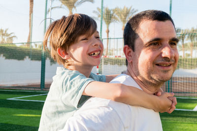 Happy father carrying son on back at sports ground