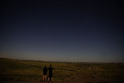 Rear view of friends standing on field against sky at night