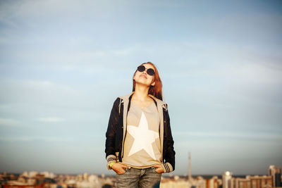 Young woman wearing sunglasses standing against sky