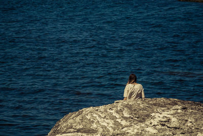 Rear view of woman sitting on rock by sea