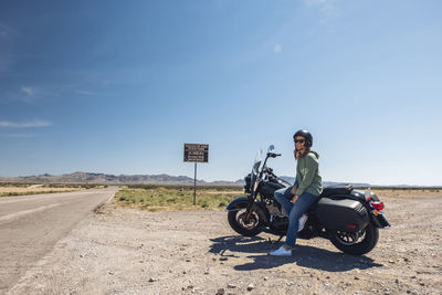 Woman sitting on motorcycle by desert road against sky during road trip, nevada, usa