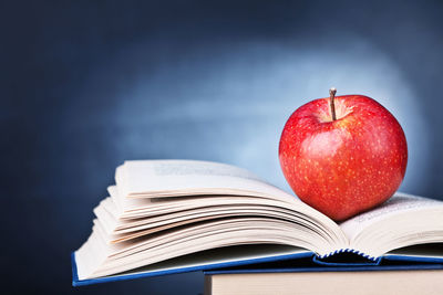 Close-up of apple on stacked books against blackboard