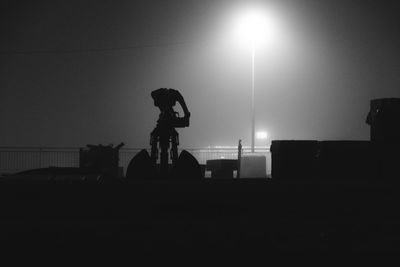 Silhouette people standing on illuminated street against clear sky at night