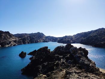 Rocks by sea against clear blue sky