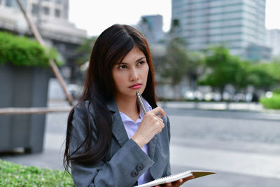 Portrait of young woman holding umbrella against buildings in city