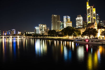 River by illuminated buildings against sky at night