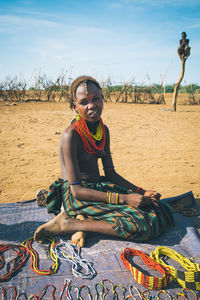 Portrait of young woman sitting on sand at beach against sky