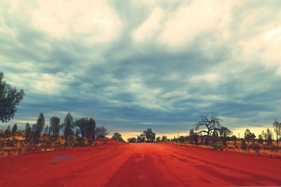 Road passing through field against cloudy sky