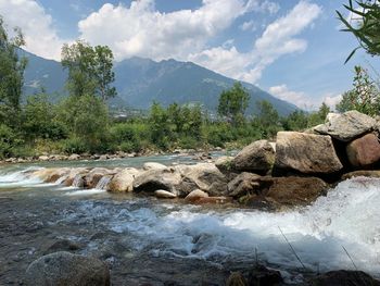 Stream flowing through rocks against sky