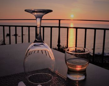 Wineglass on table by sea against sky during sunset