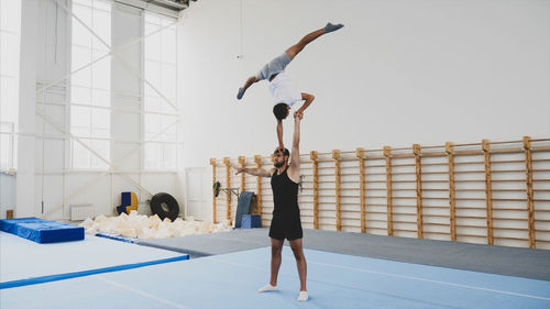 Instructor with teenage boy practicing gymnastics in club