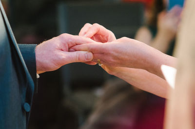 Cropped image of bride wearing wedding ring to groom at ceremony