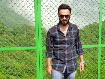 Portrait of young man standing against chainlink fence