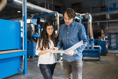 Inspector working over document with colleague while standing in industry